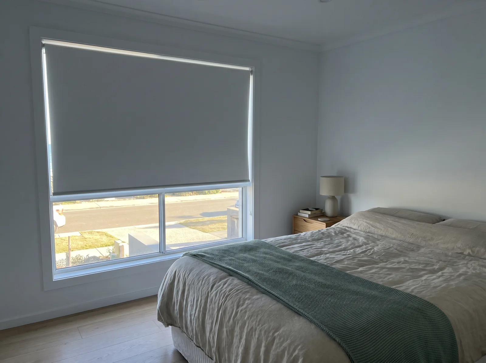 Dim, restful bedroom behind a fully lowered blockout blind while morning sun blazes outside